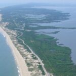 Luftaufnahme einer Küstenlandschaft mit Sandstränden und grünen Flächen entlang der Küste.