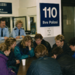 Im Polizeirevier Berlin-Plötzensee sitzen dänische Gäste mit Polizei Berlin am Tisch, vor einem Schild „110“ und in blauen Uniformen.